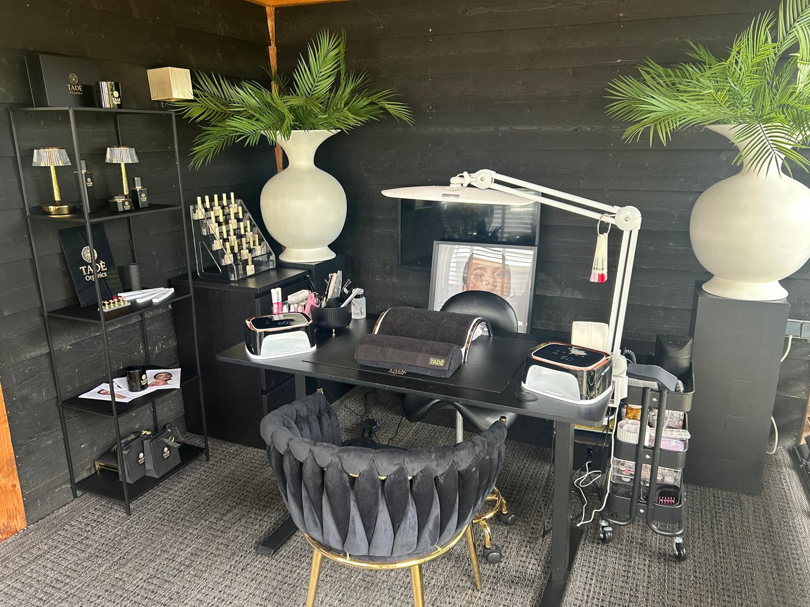 Nagelstudio Tadè Organics met zwarte manicuretafel, stoel met gouden poten en hoge palmbladeren